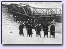 Niemieccy żołnierze na tle uszkodzonych mostów na Kanale Młyńskim. Po prowizorycznej konstrukcji saperskiej wyjeżdża parowóz w kierunku Kruklanek.